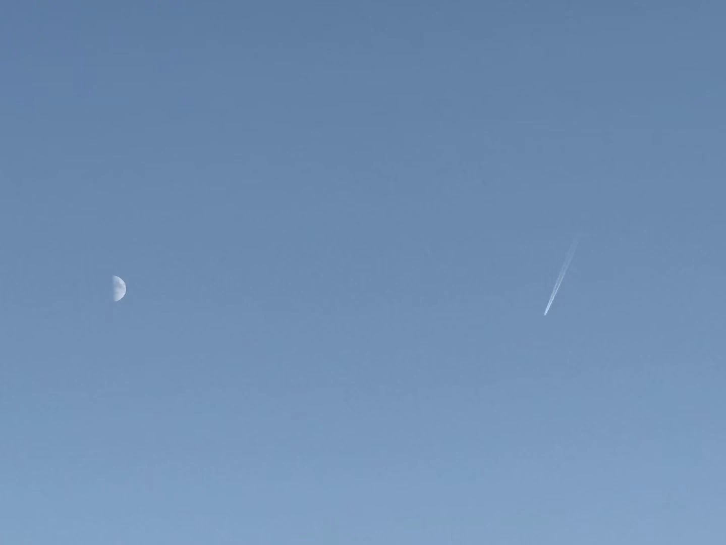 A small moon and a faint trail in a blue sky