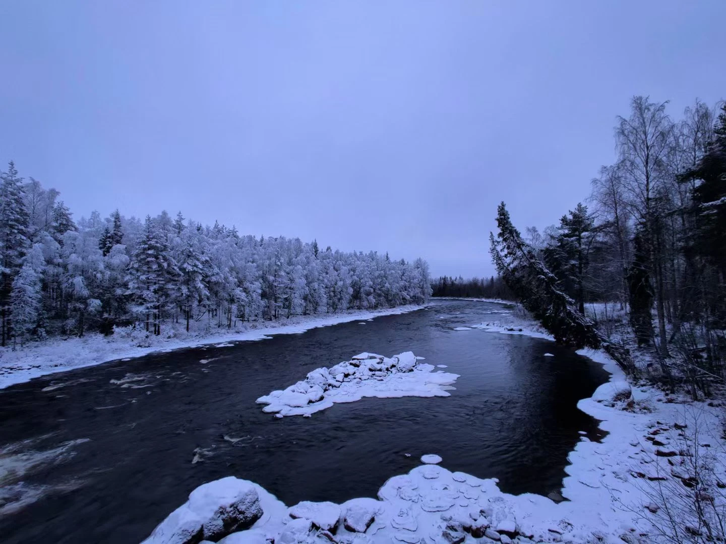A dark river winding through snow-covered trees in Finland